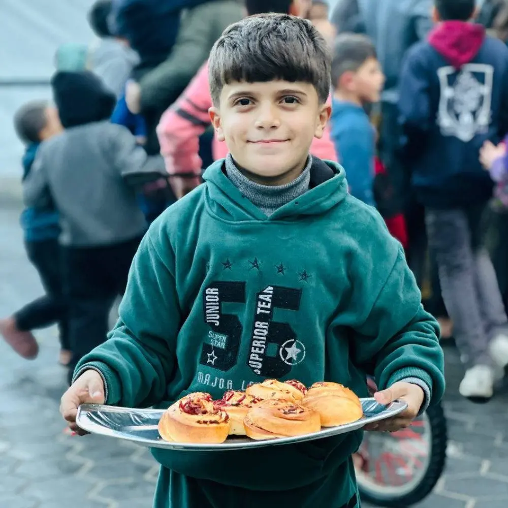 Child holding a tray of fresh pastries during a food distribution event in Palestine by Giving Hands Canada
