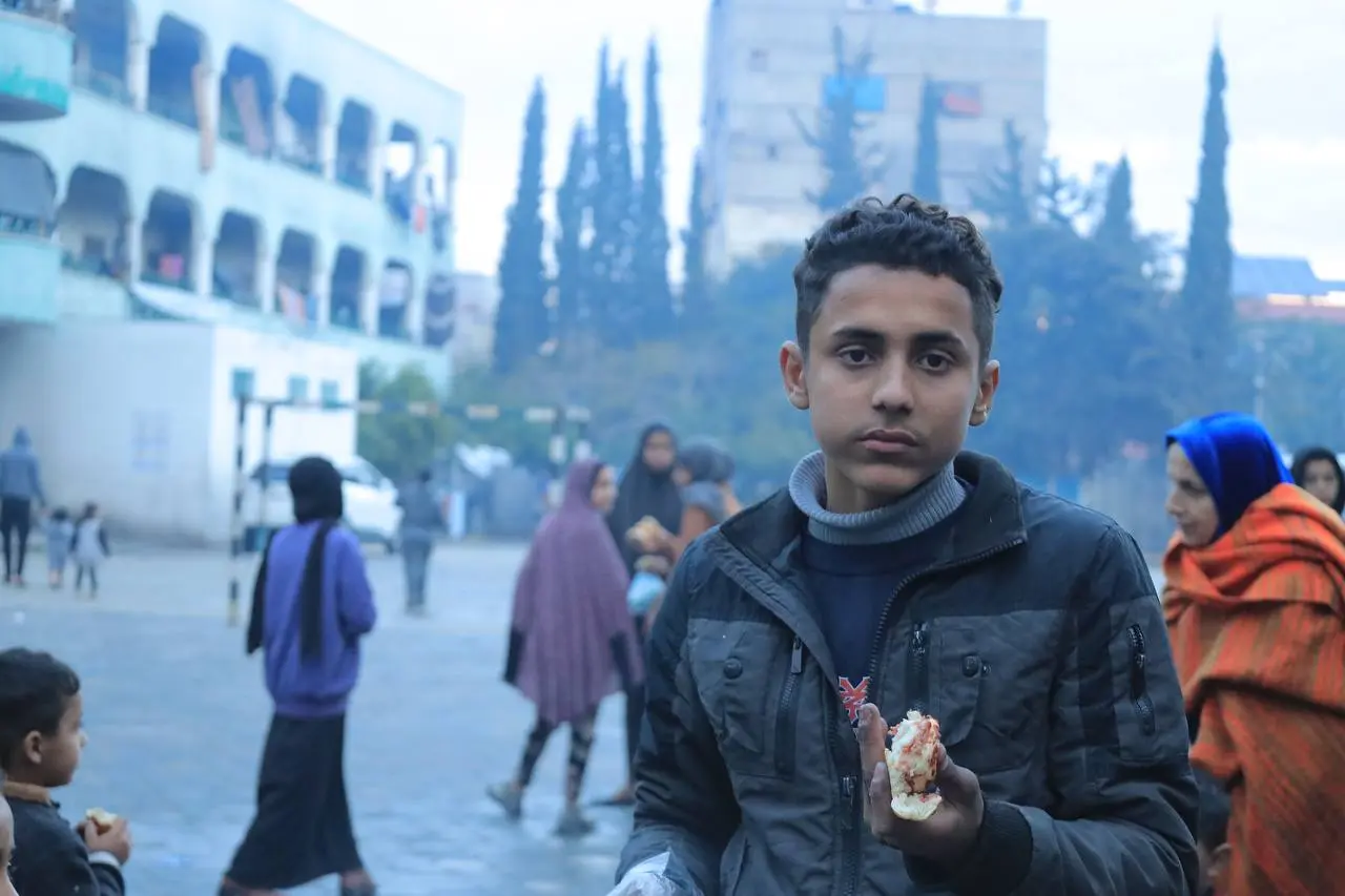 Young person holding bread in an outdoor area during a food aid distribution in Palestine by Giving Hands Canada