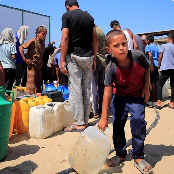 Children and adults wait with water containers at a Giving Hands emergency water distribution site.